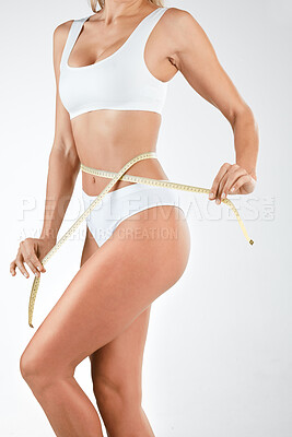 Buy stock photo Shot of a woman measuring her waist using a tape measure against a studio background