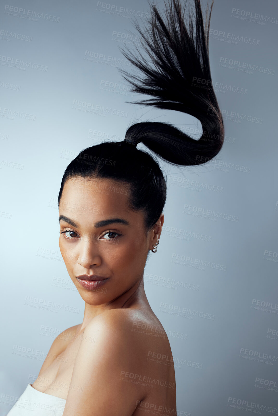 Buy stock photo Studio shot of an attractive young woman holding her hair against a grey background