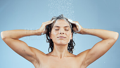 Buy stock photo Studio shot of an attractive young woman washing her hair while taking a shower against a blue background