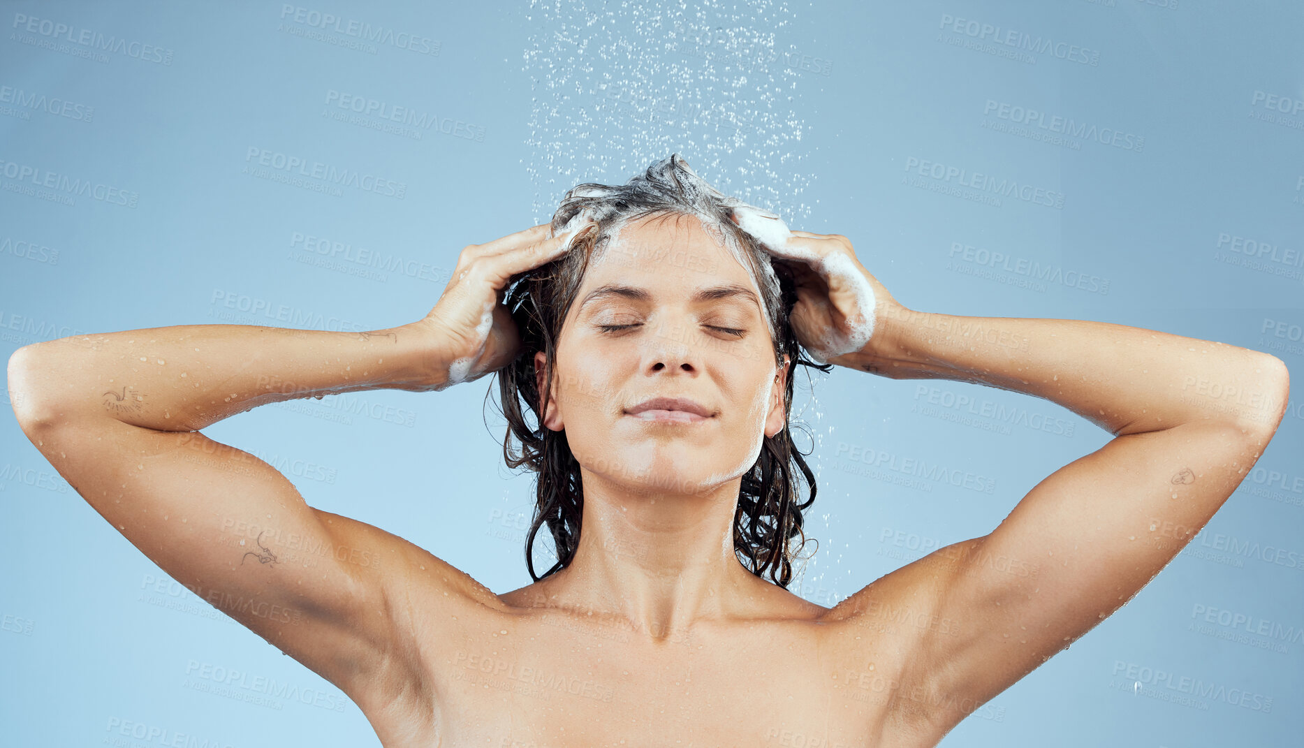 Buy stock photo Studio shot of an attractive young woman washing her hair while taking a shower against a blue background