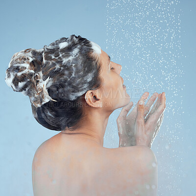 Buy stock photo Studio shot of an attractive young woman washing her hair while taking a shower against a blue background