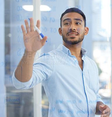 Buy stock photo Shot of a young businessman writing notes on a glass wall in an office