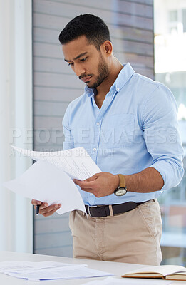 Buy stock photo Shot of a young businessman going through paperwork in an office