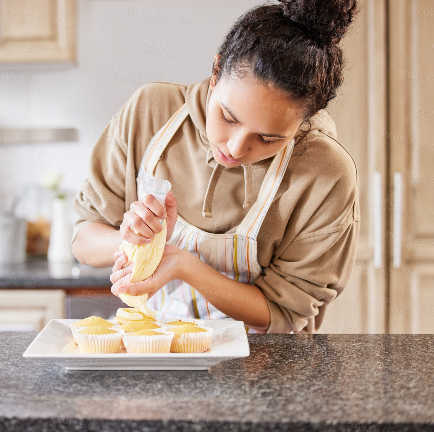 Buy stock photo Shot of a young woman frosting freshly baked cupcakes