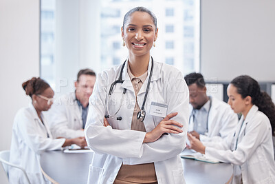 Buy stock photo Cropped portrait of an attractive young female doctor standing in the boardroom with her arms folded with her colleagues in the background