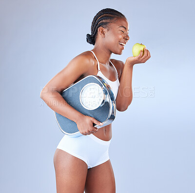 Buy stock photo Studio shot of a young woman eating an apple and holding weighing scale under her arm