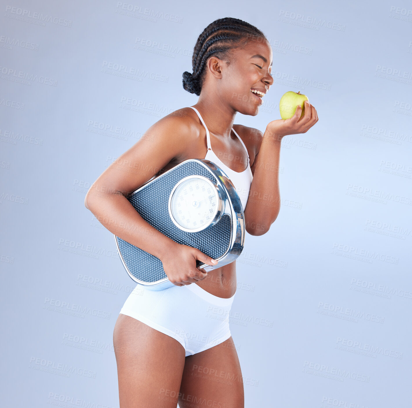 Buy stock photo Studio shot of a young woman eating an apple and holding weighing scale under her arm