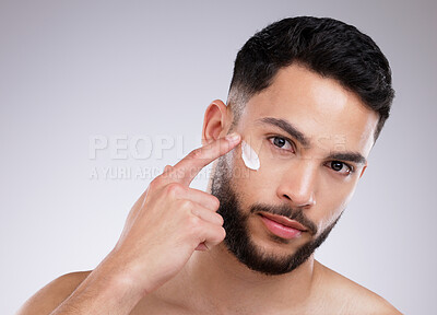 Buy stock photo Shot of a handsome young man applying moisturiser on his face against a studio background