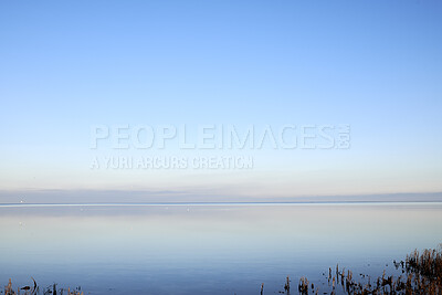 Buy stock photo Sea at sunset with clear blue sky making a nature mirror reflection on the water with golden grey clouds on the horizon at dusk. Copy space, wallpaper background of beautiful and colorful ocean view