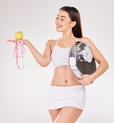 Buy stock photo Studio shot of an attractive young woman posing with an apple, measuring tape and weightscale against a grey background