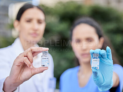 Buy stock photo Shot of two doctors holding vaccine vials against a city background
