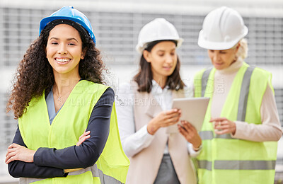 Buy stock photo Cropped portrait of an attractive young female engineer standing with her arms folded with her colleagues in the background on a construction site