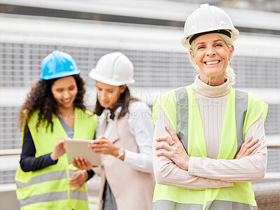 Buy stock photo Cropped portrait of an attractive mature female engineer standing with her arms folded with her colleagues in the background on a construction site
