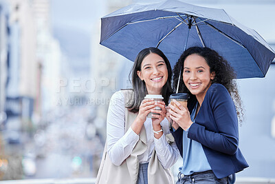 Buy stock photo Portrait of two young businesswomen drinking coffee while standing together under an umbrella in the city