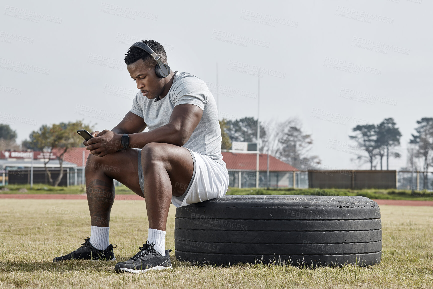 Buy stock photo Shot of a sporty young man wearing his headphones while out for a workout