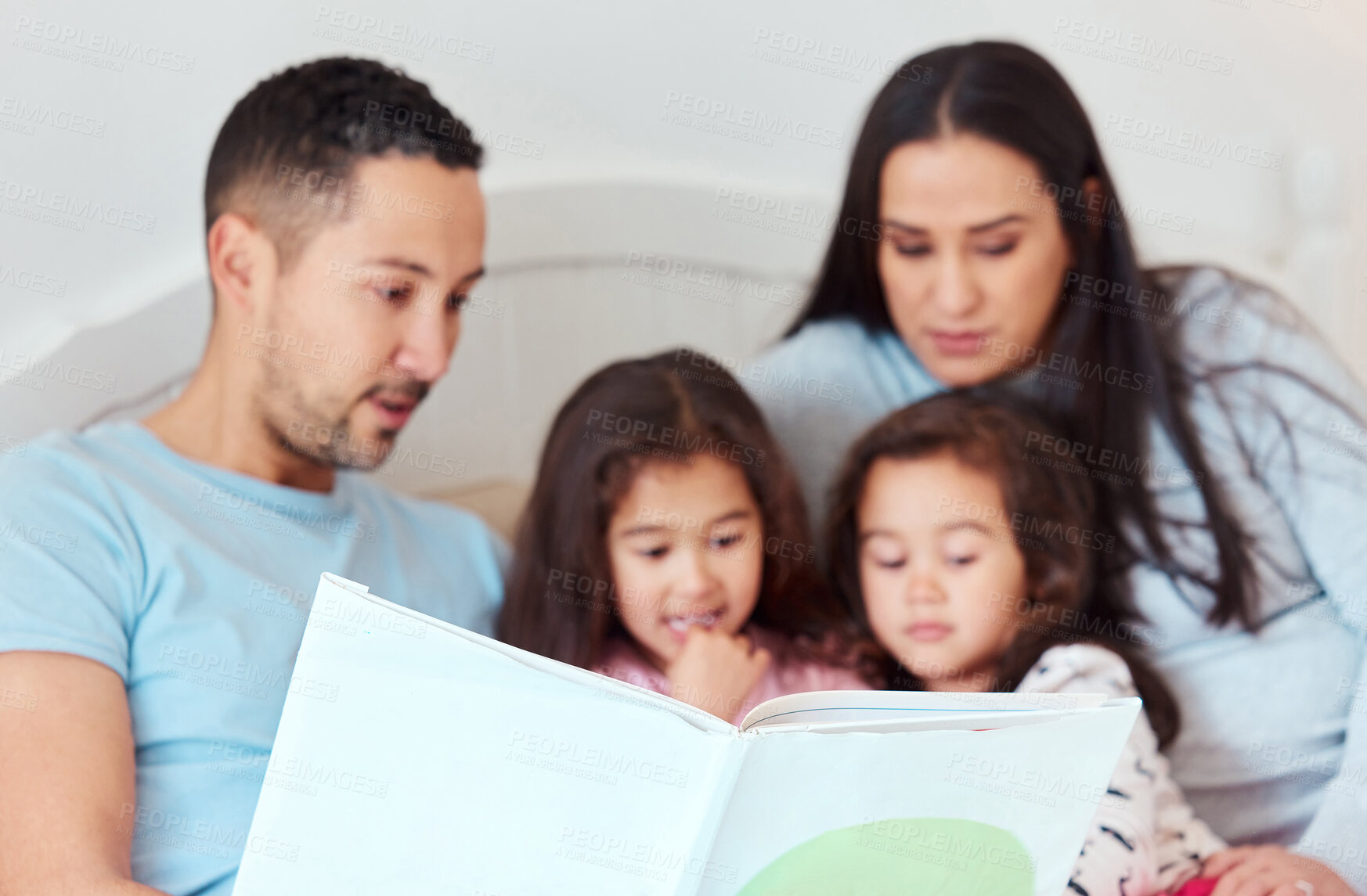 Buy stock photo Shot of a man holding a storybook while sitting with his wife and two daughters