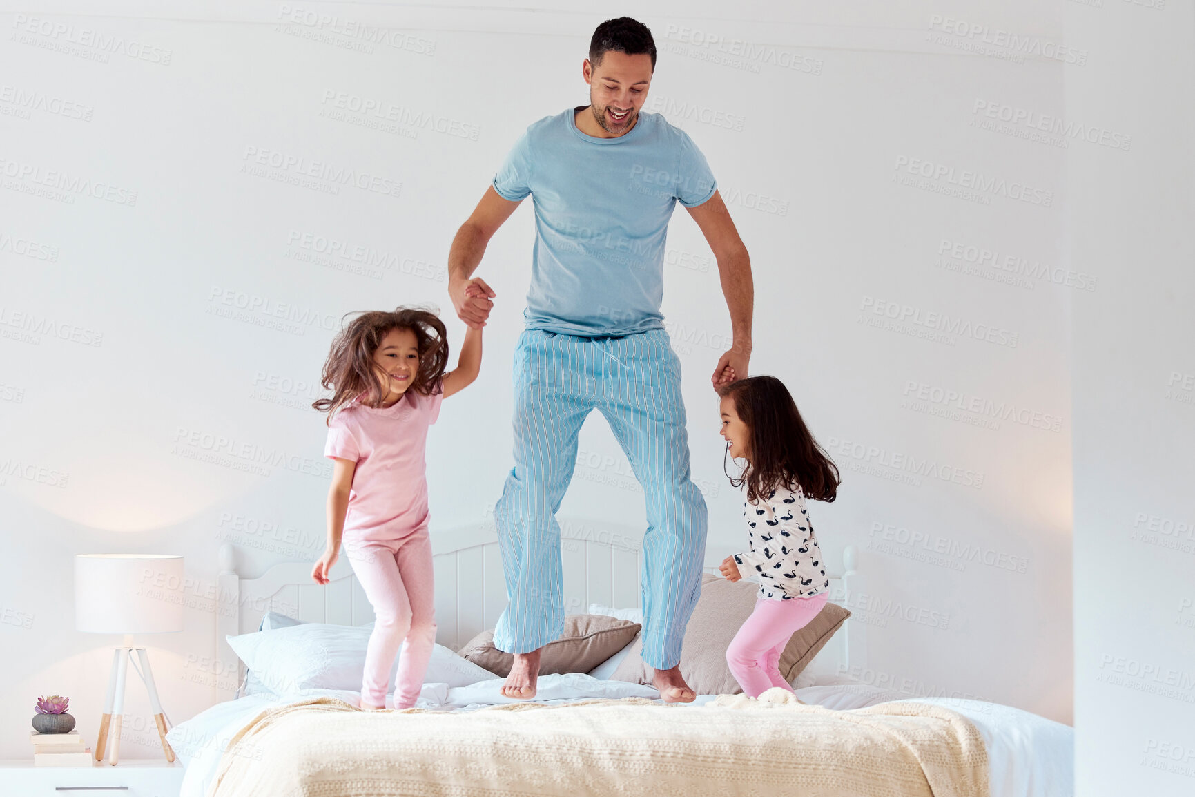 Buy stock photo Shot of a man jumping on a bed with his two daughters