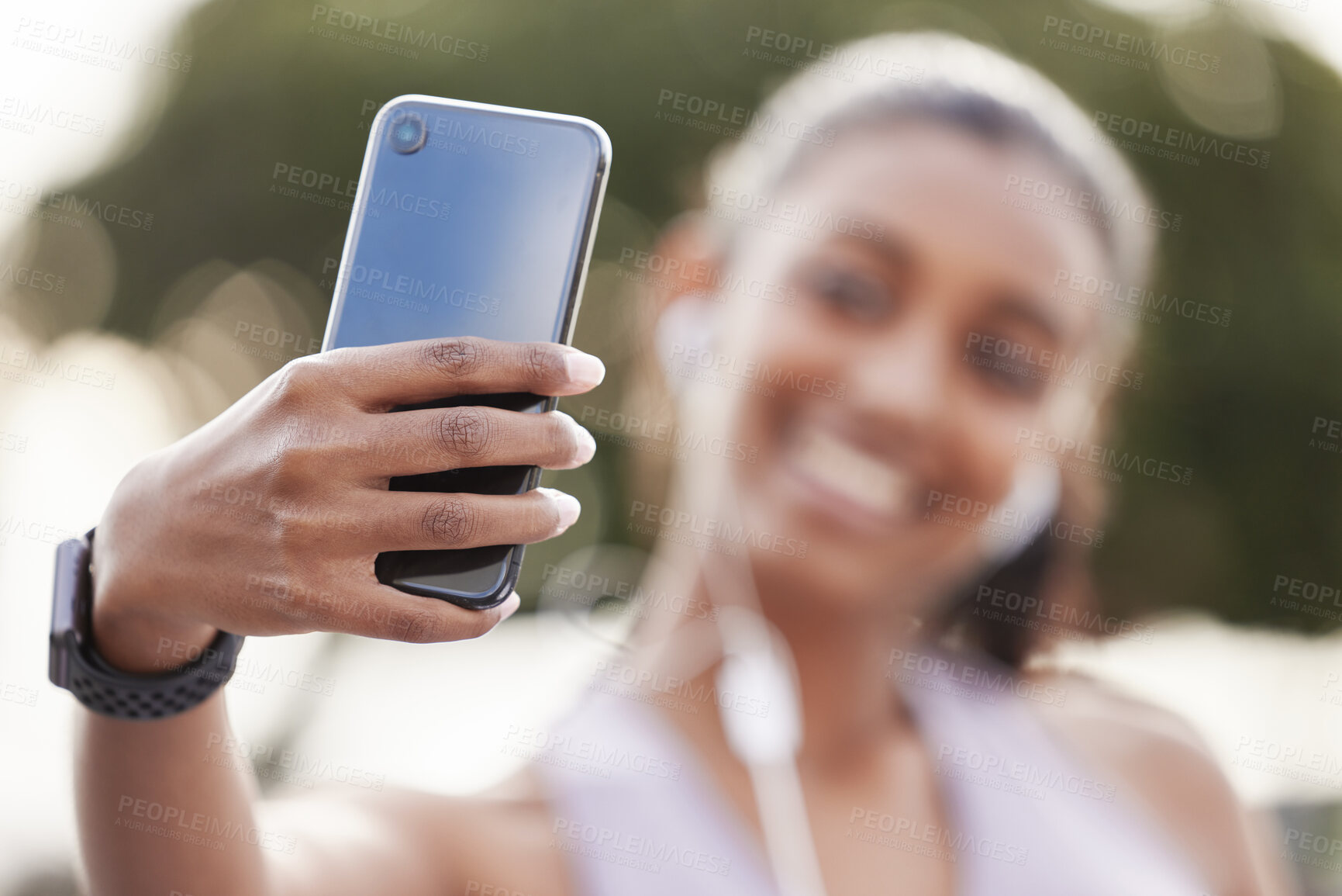 Buy stock photo Closeup shot of a sporty young woman wearing earphones and taking selfies while exercising outdoors