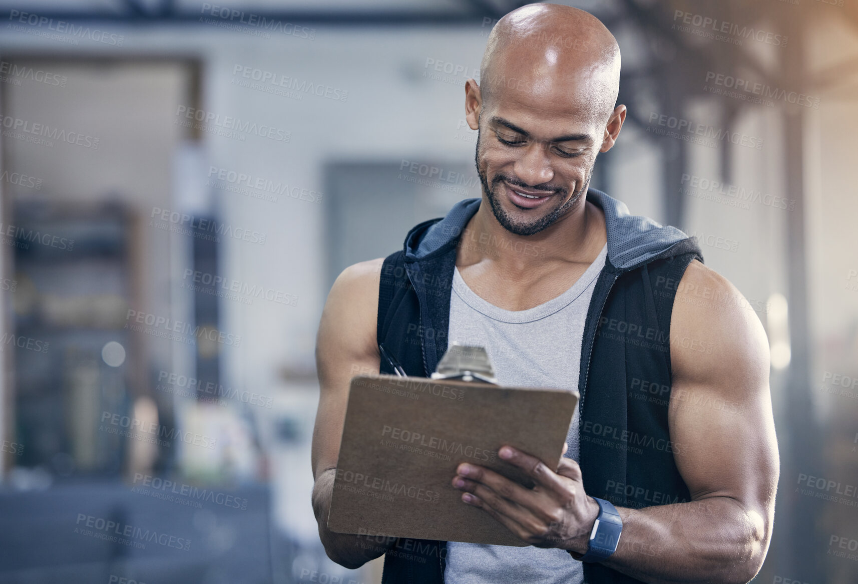 Buy stock photo Shot of a muscular young man writing notes on a clipboard while working in a gym