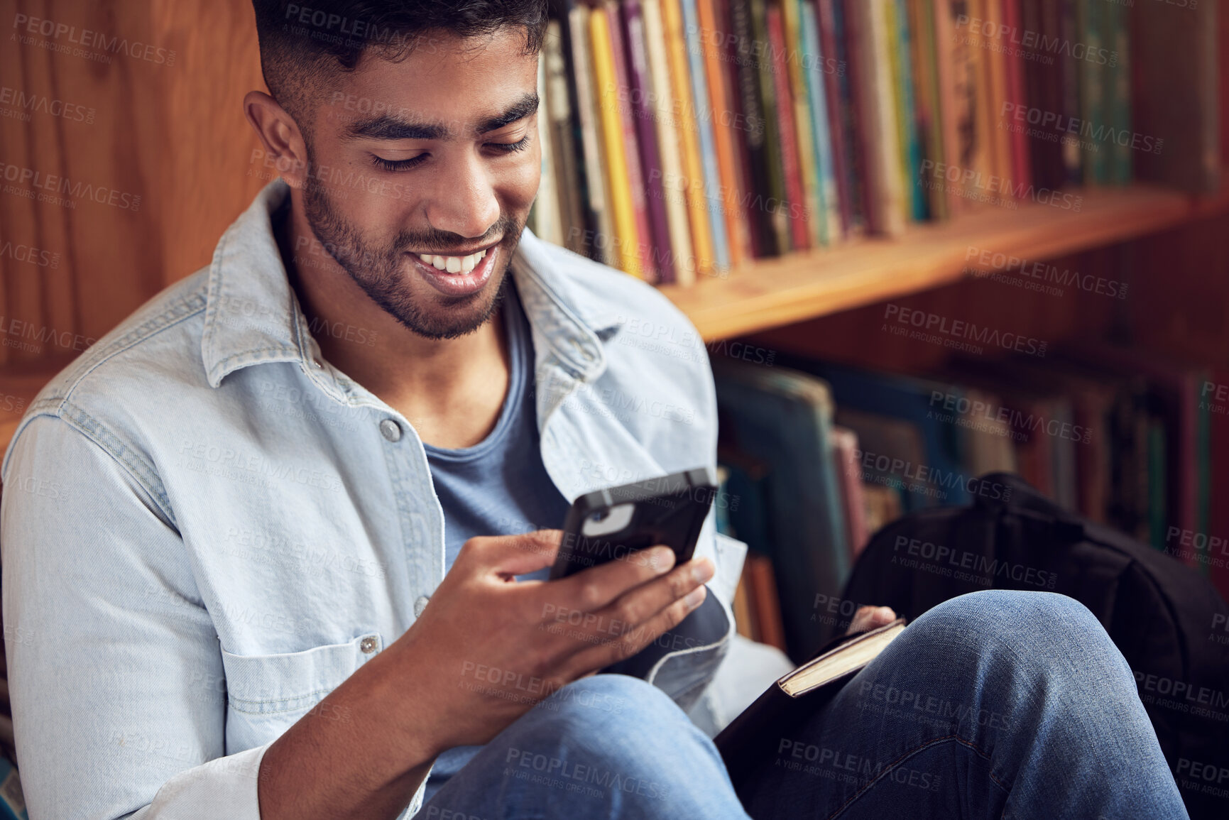 Buy stock photo Shot of a young man using a smartphone in a library at university