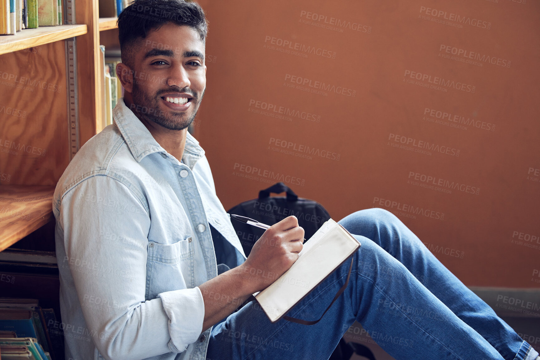 Buy stock photo Shot of a young man making notes in a library at university