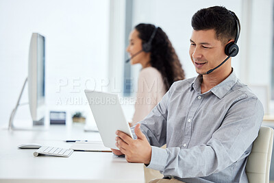 Buy stock photo Shot of a young call centre agent working on a digital tablet in an office with his colleague in the background