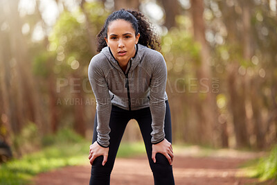 Buy stock photo Shot of a fit young woman resting with her hands on her knees while out for a run