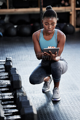 Buy stock photo Shot of a fit young woman using a digital tablet in a gym