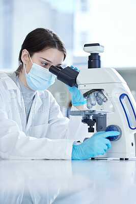 Buy stock photo Shot of a young woman using a microscope in a lab