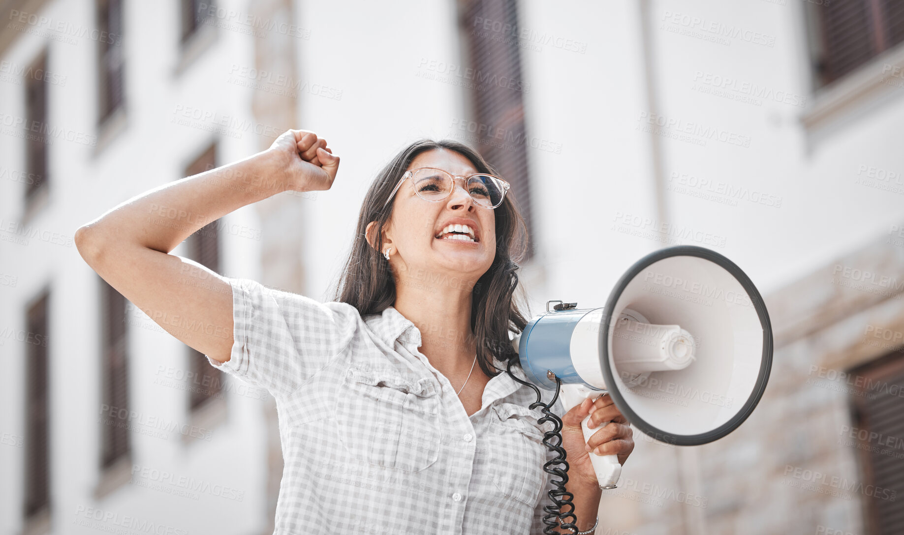 Buy stock photo Shot of a young woman screaming into a loud speaker while protesting in the city