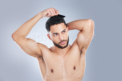 Buy stock photo Studio shot of a handsome young man combing his hair against a grey background