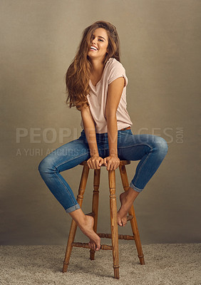 Buy stock photo Studio shot of a beautiful young woman sitting on a stool against a plain background