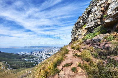 Buy stock photo Beautiful scenic view of mountains and a hiking or walking trail surrounded by foliage, plants and greenery on a sunny spring day. Landscape covered in rocks and flora with cloudy blue sky copy space