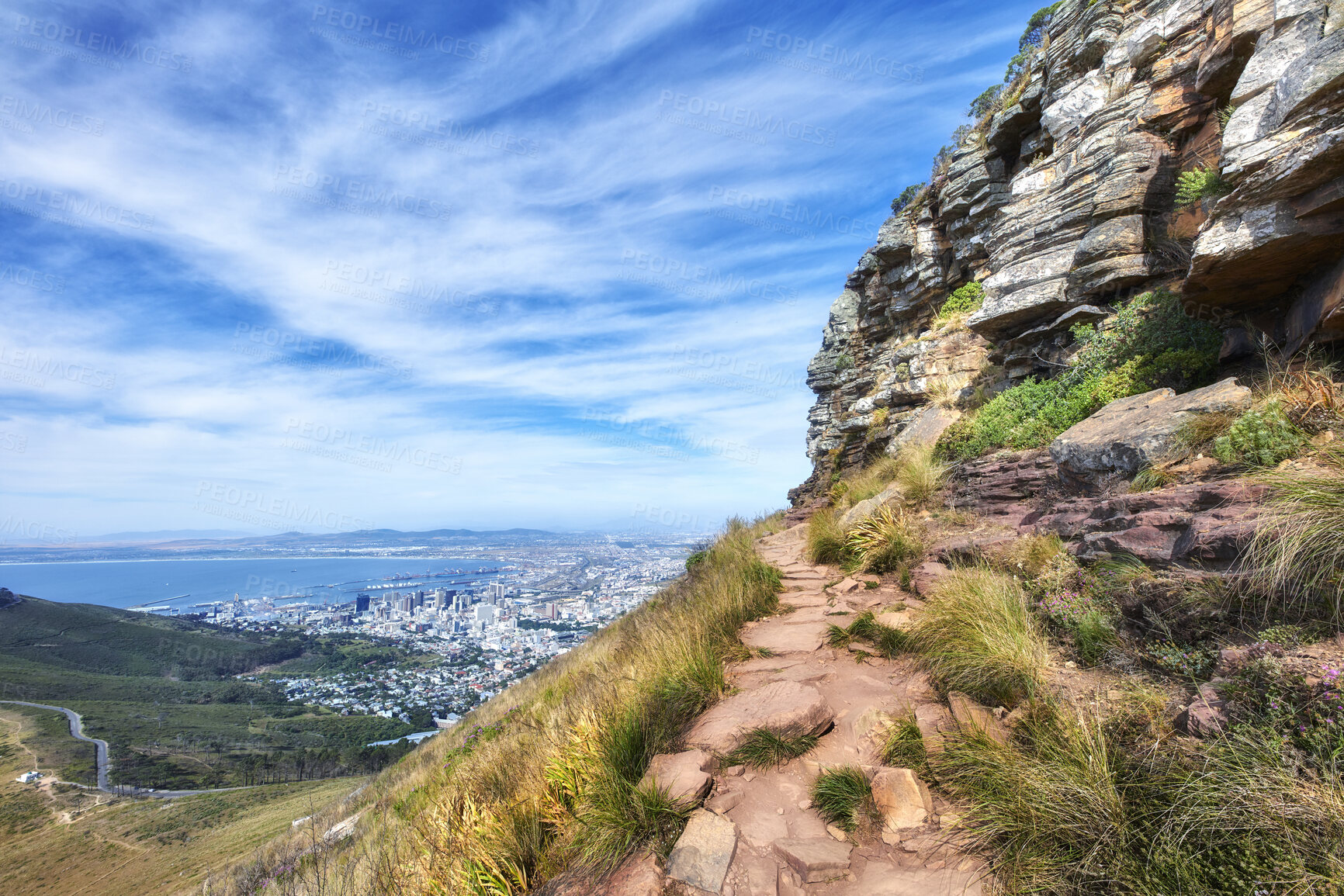 Buy stock photo Beautiful scenic view of mountains and a hiking or walking trail surrounded by foliage, plants and greenery on a sunny spring day. Landscape covered in rocks and flora with cloudy blue sky copy space