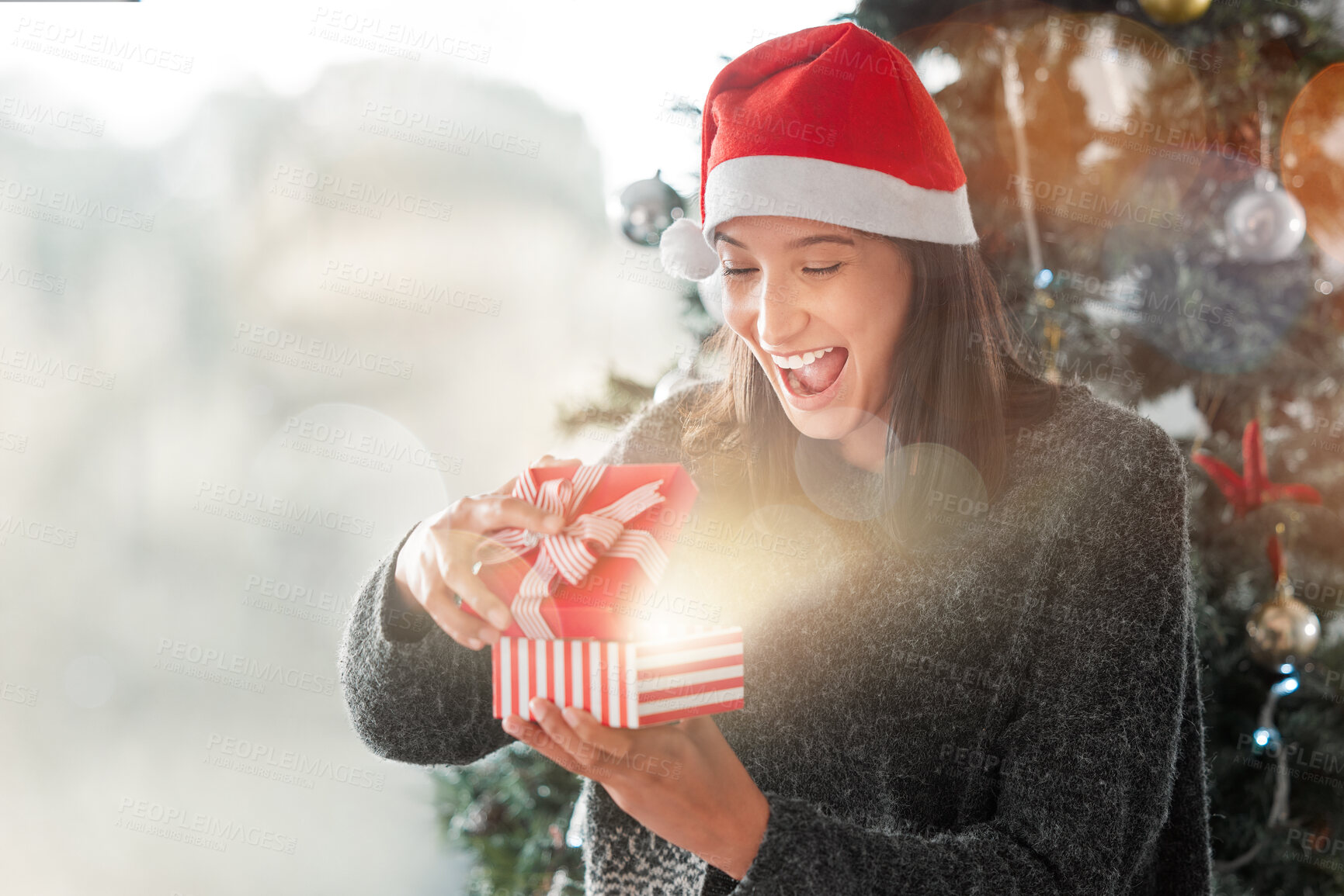 Buy stock photo Shot of a young woman opening a Christmas gift at home