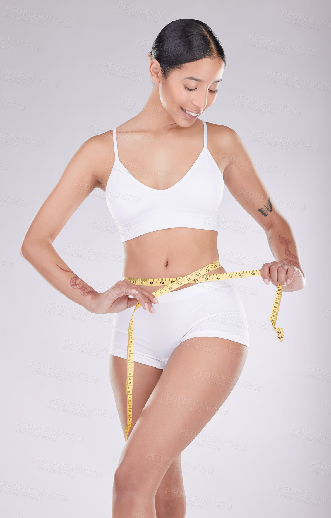 Buy stock photo Shot of an attractive young woman standing in the studio and using a measuring tape around her waist