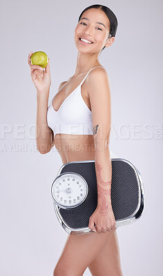 Buy stock photo Shot of an attractive young woman standing and alone posing with an apple and a scale in the studio