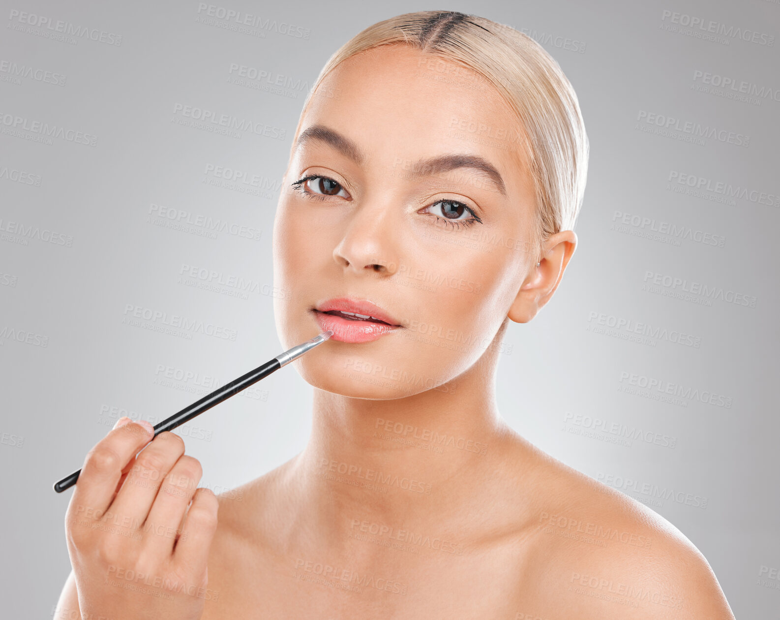 Buy stock photo Shot of a beautiful young woman applying lipgloss to her lips against a grey background