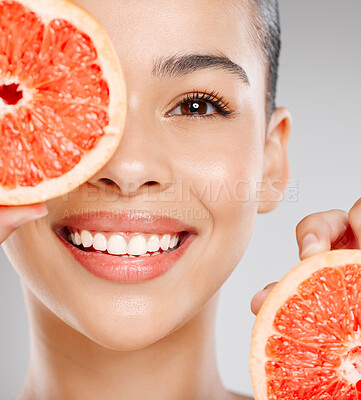 Buy stock photo Studio shot of an attractive young woman holding grapefruit to her face against a grey background