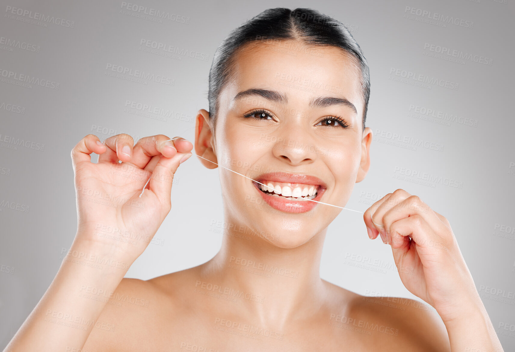 Buy stock photo Studio shot of an attractive young woman flossing her teeth against a grey background