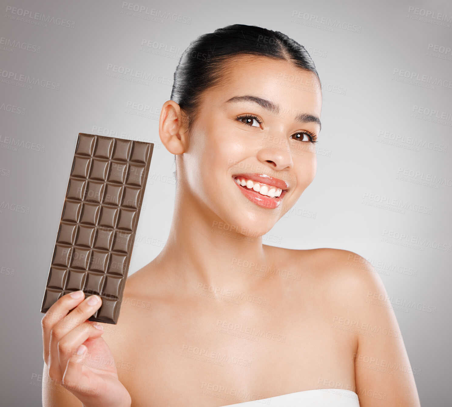 Buy stock photo Studio shot of an attractive young woman eating a slab of chocolate against a grey background