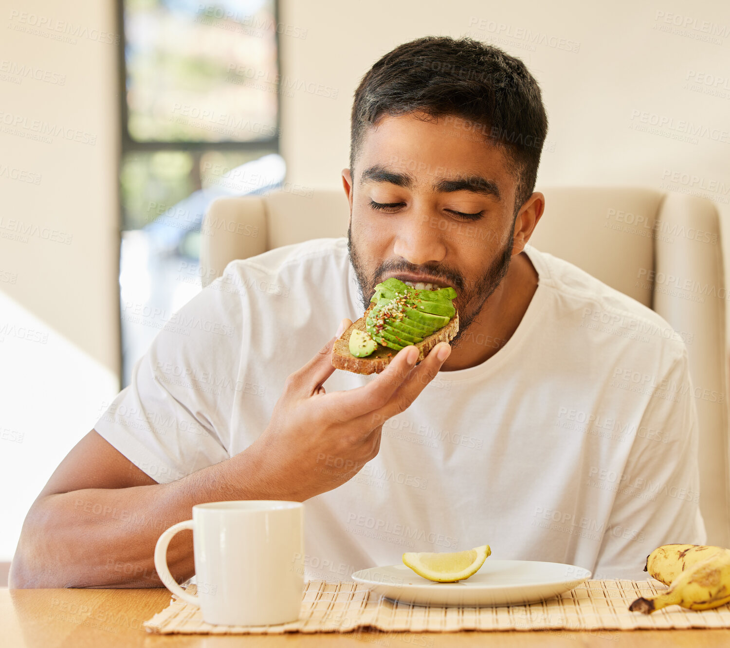 Buy stock photo Man, breakfast and eating bread, avocado toast and healthy meal for morning, energy and nutrition at home. Hungry young guy bite food, sandwich and vegan diet at table for brunch, fiber and protein