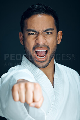 Buy stock photo Cropped portrait of a handsome young male martial artist practicing karate in studio against a dark background