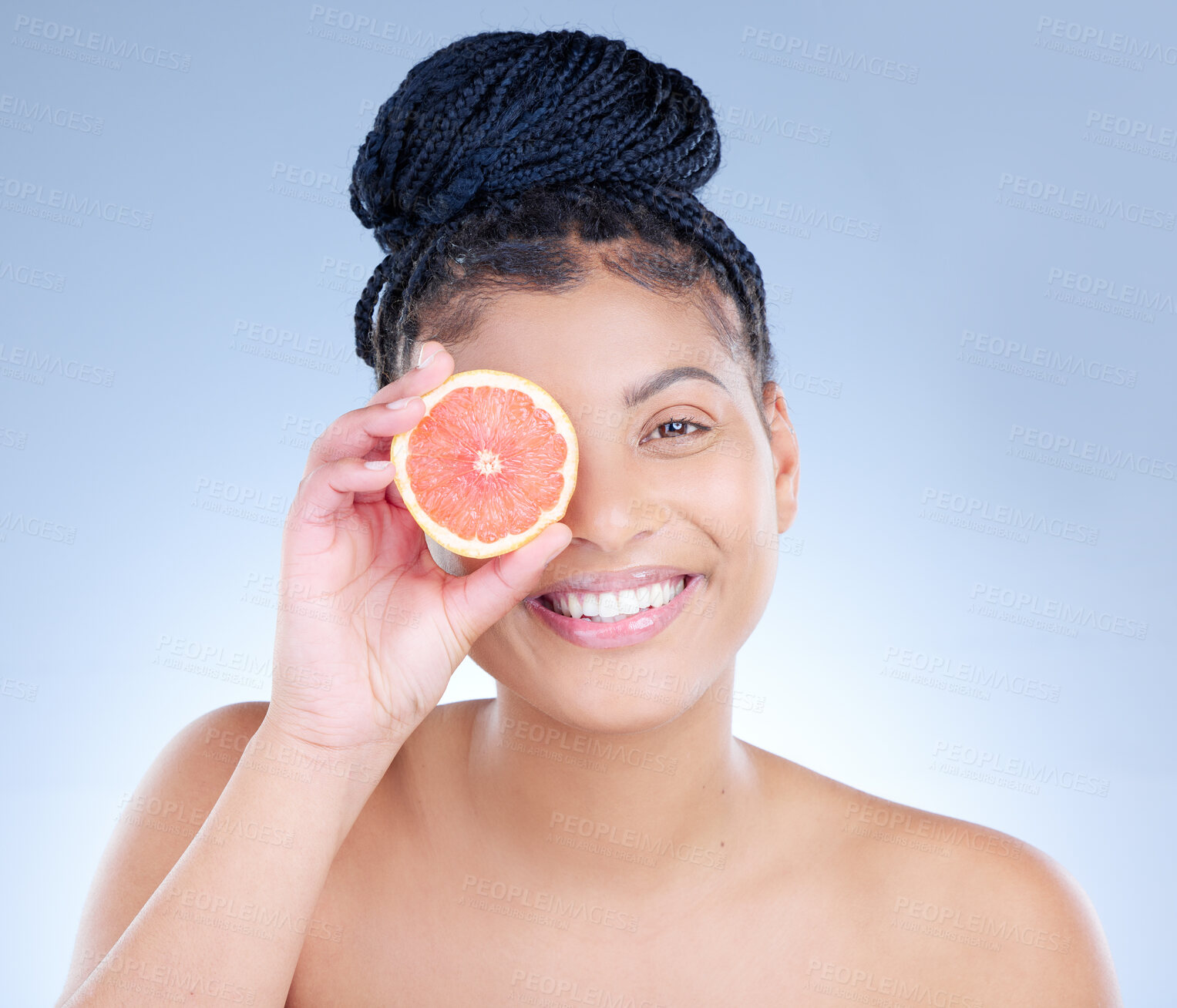 Buy stock photo Studio portrait of an attractive young woman holding a sliced grapefruit against a blue background