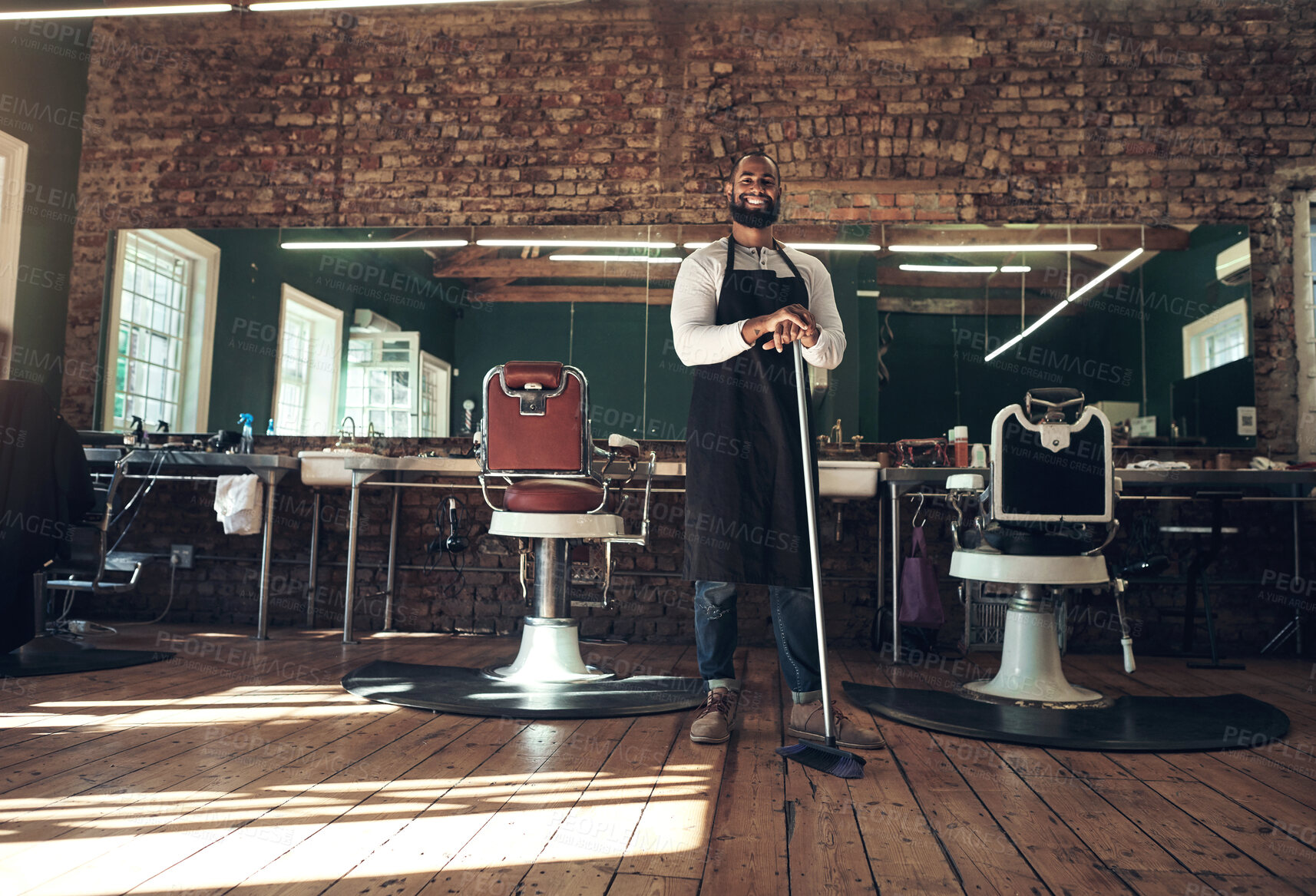 Buy stock photo Full length shot of a handsome young barber standing alone in his salon and holding a broom