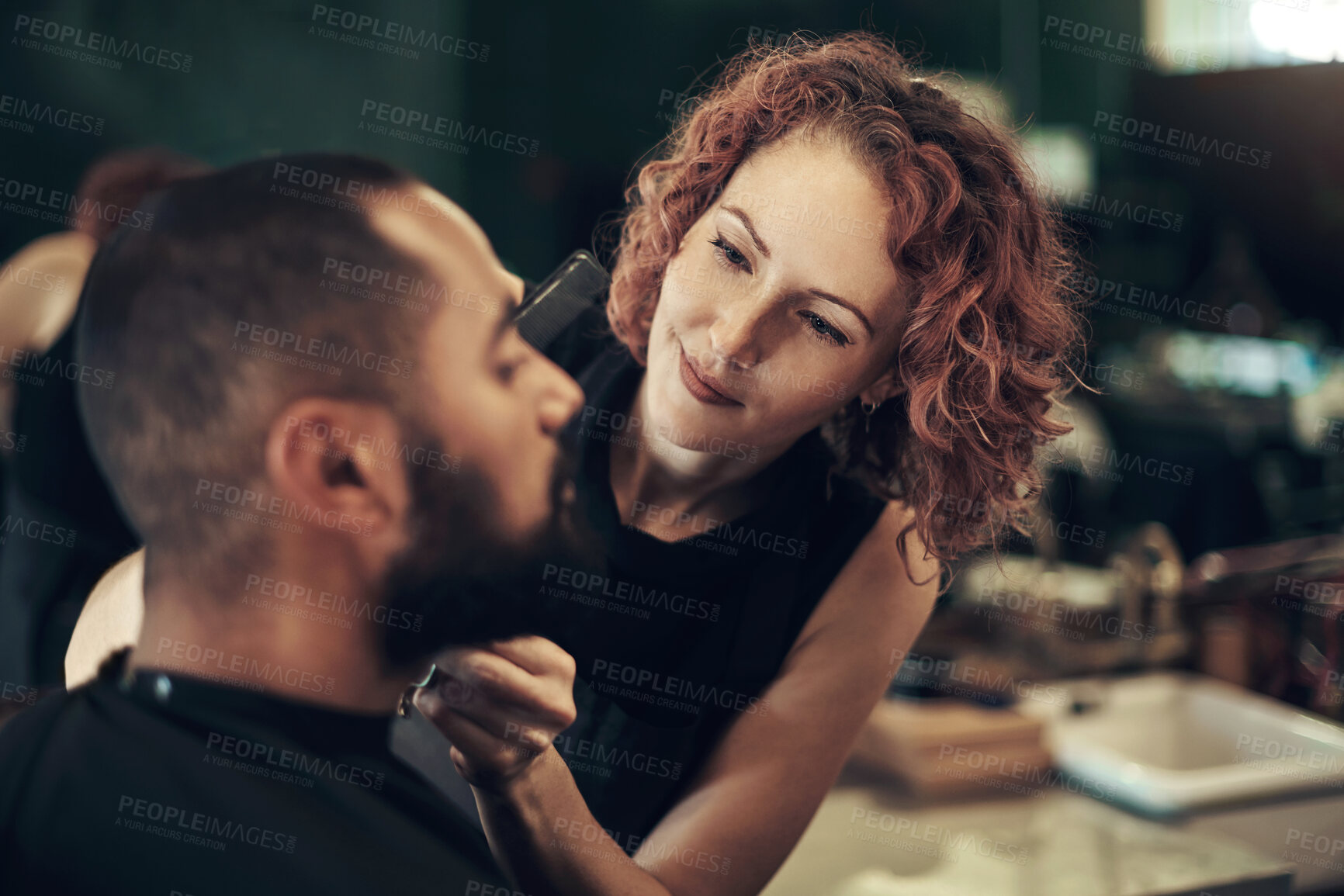 Buy stock photo Shot of an attractive young hairdresser standing and styling her client's beard in her salon