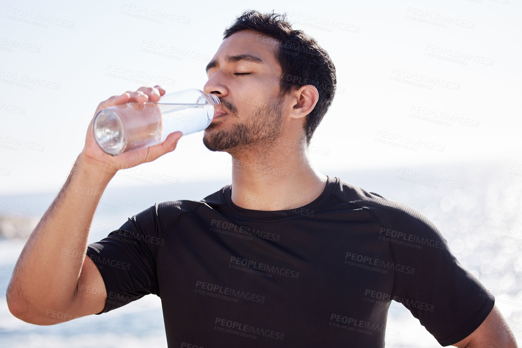 Buy stock photo Cropped shot of a handsome young male athlete hydrating during his workout on the beach