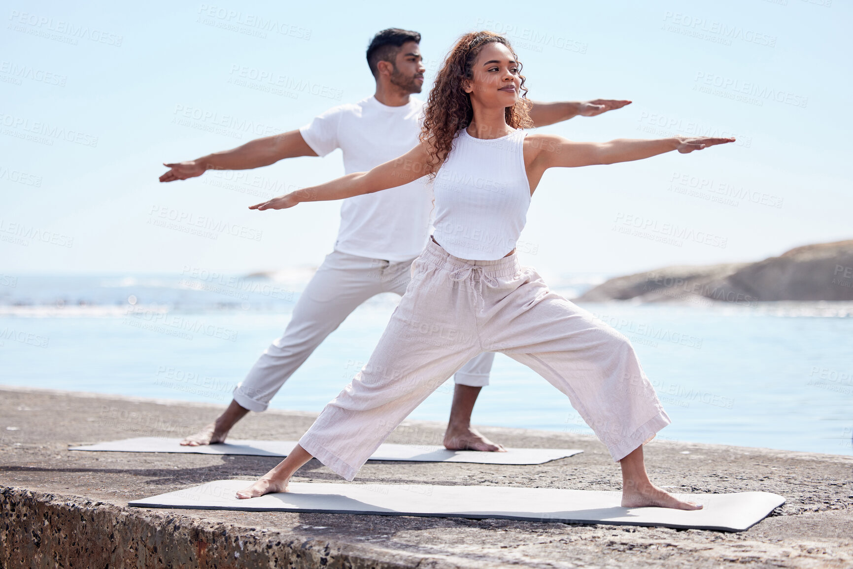 Buy stock photo Couple yoga, beach and exercise outdoor in nature for fitness workout and wellness. African woman and a man at ocean for warrior pose, stretching or pilates training for peace, freedom or mindfulness