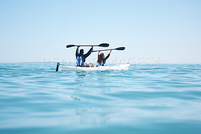 Buy stock photo Rearview of a young couple raising their oars while kayaking together at a lake