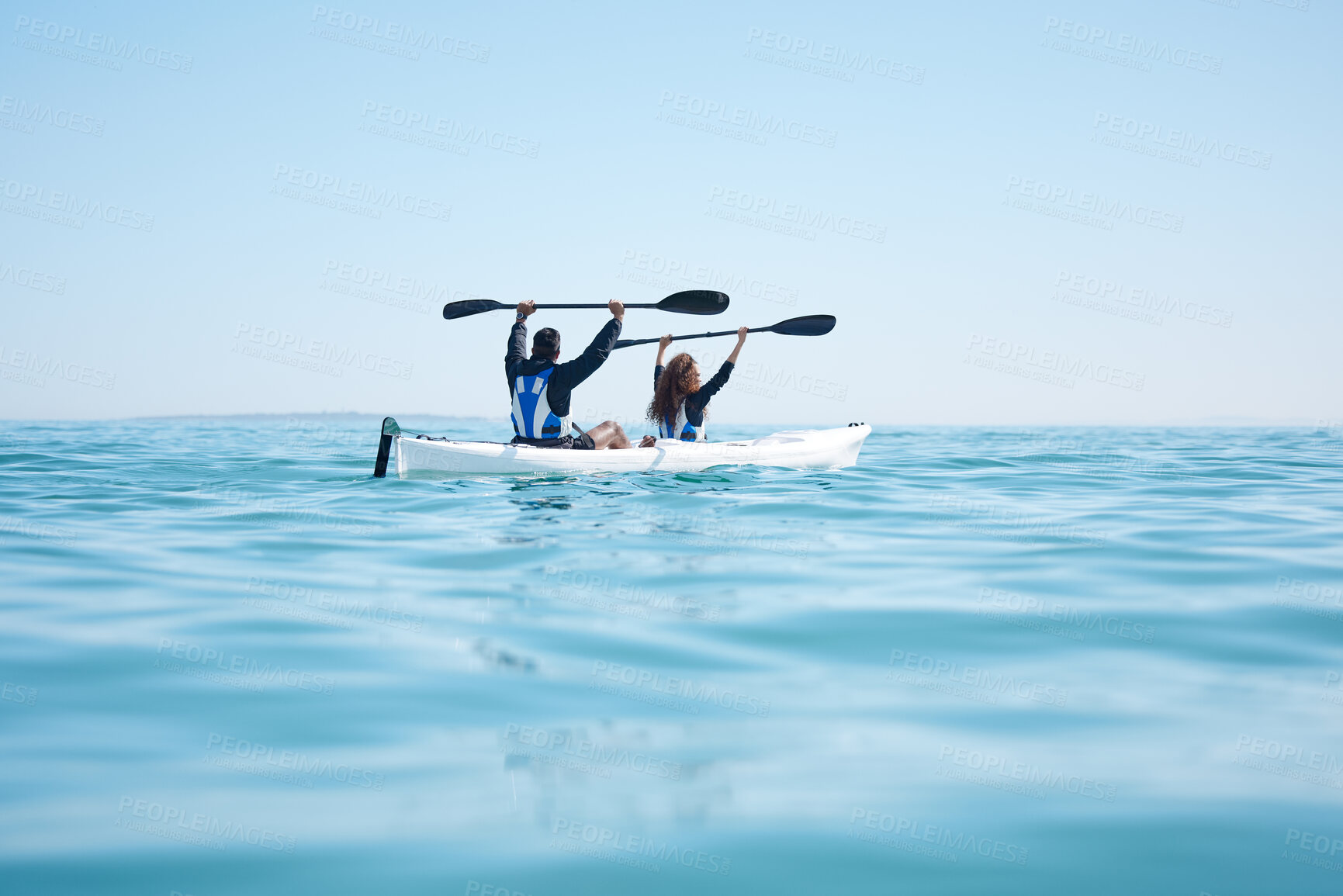 Buy stock photo Rearview of a young couple raising their oars while kayaking together at a lake